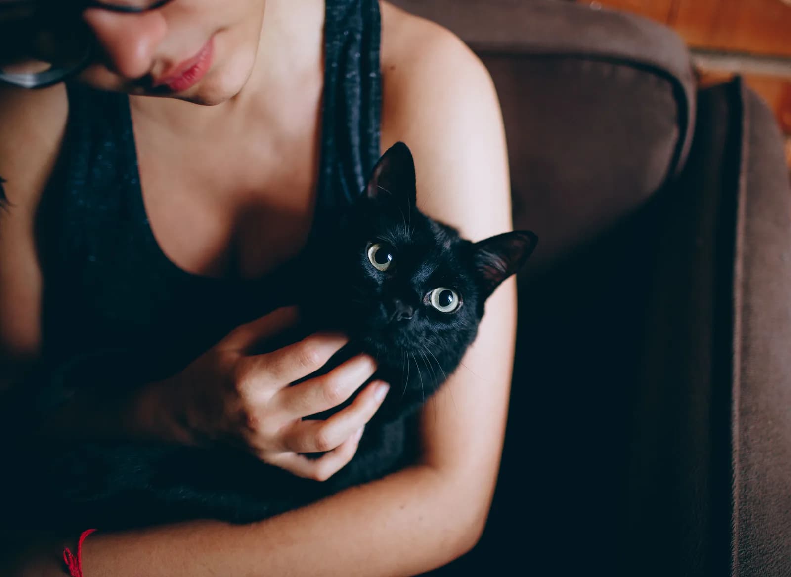 A young woman holding a black kitten against her chest, the kitten looking straight at the camera.
