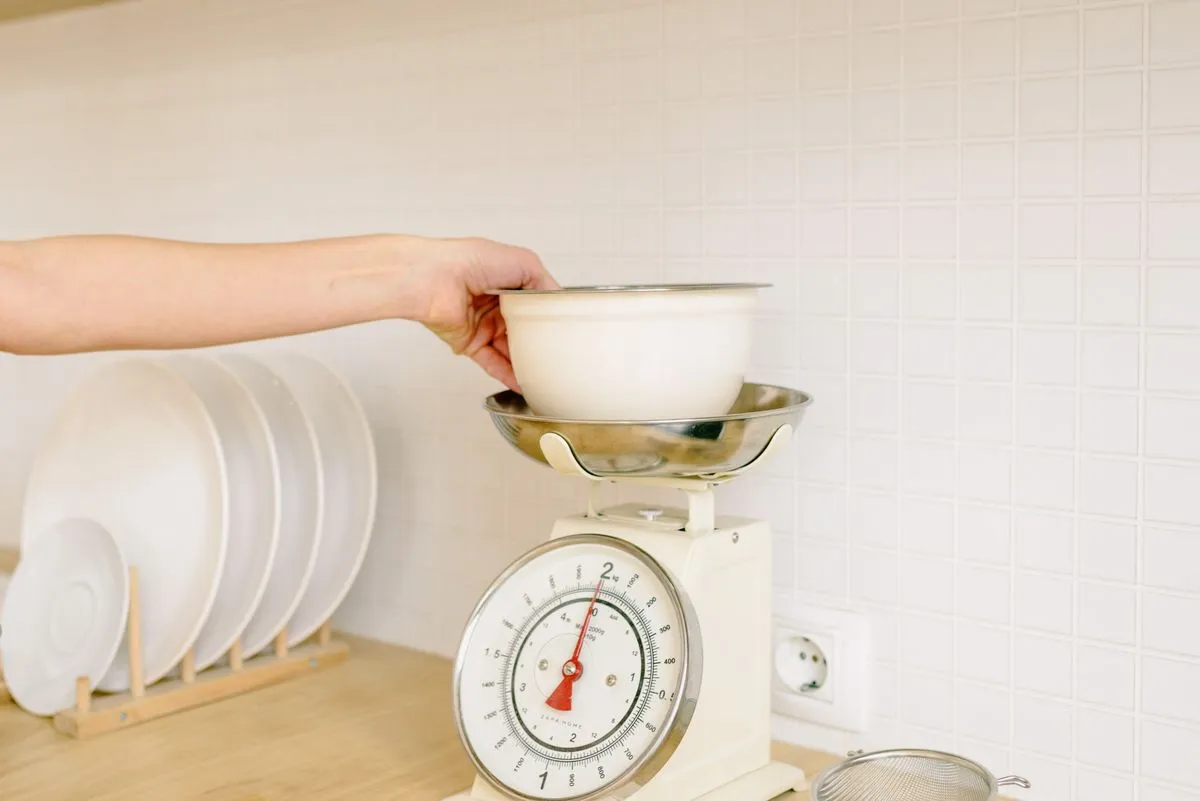 A hand weighing a bowl of food on a kitchen scale